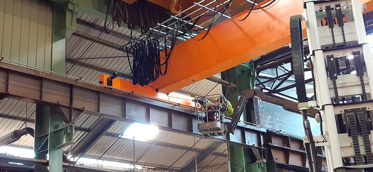 Opérateur en nacelle intervenant sur un pont roulant orange en hauteur dans une usine