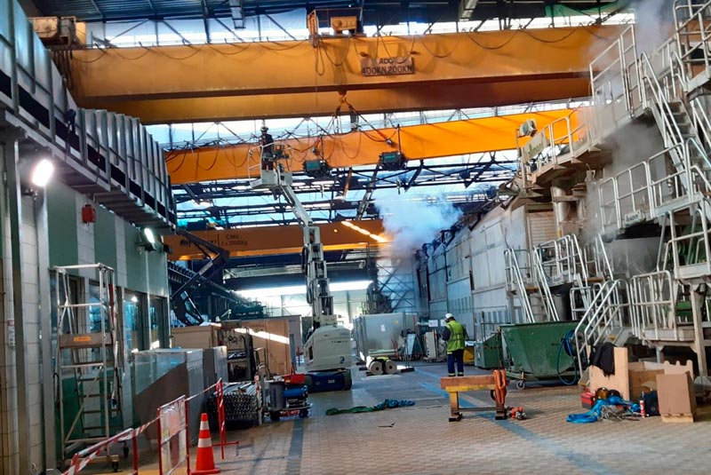 Ponts roulants double poutre oranges dans un hall industriel avec technicien et nacelle