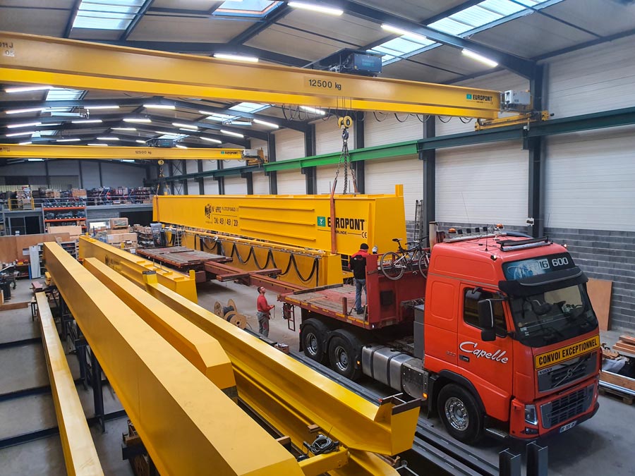 Atelier avec poutres de ponts roulants jaunes EUROPONT et pont roulant chargé sur un camion rouge